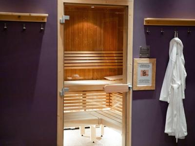 Interior view of a wooden sauna with benches and a white robe hanging on a purple wall.