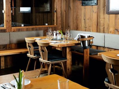 Restaurant confortable avec murs en bois, table avec chaises et banquette d'angle, dressée avec verres et couverts.