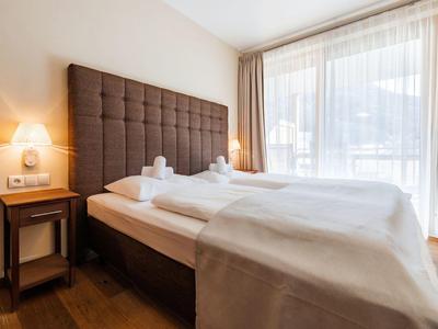 Cozy hotel room with a double bed, brown headboard, wooden floor, and sheer curtains.
