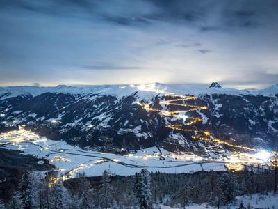 Snow-covered mountain village illuminated at night under cloudy sky
