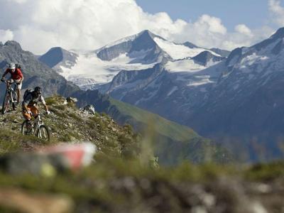 Two mountain bikers on a rocky trail with snowy mountain peaks in the background