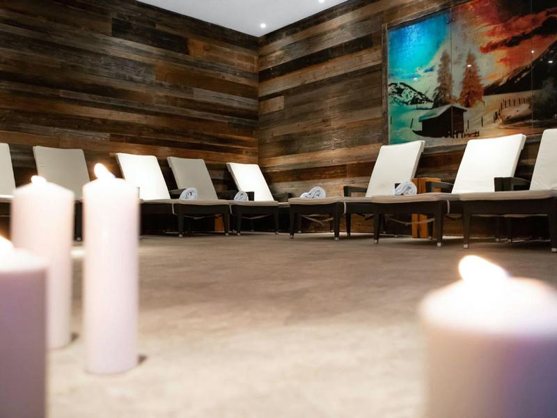 Calm lounge area with wooden walls, white chairs, and lit candles creating a relaxing atmosphere.