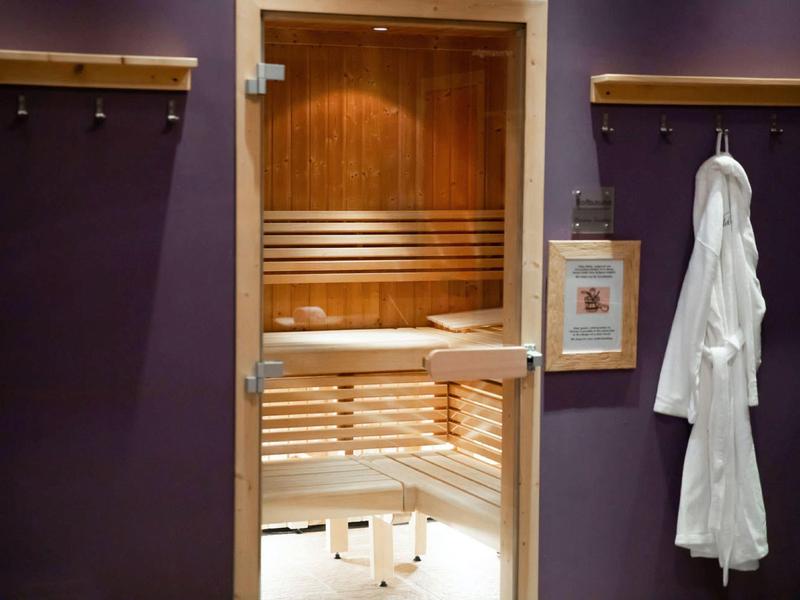 Interior view of a wooden sauna with benches and a white robe hanging on a purple wall.