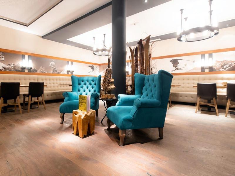 Modern hotel lounge with turquoise armchairs, wooden accents, and warm lighting.