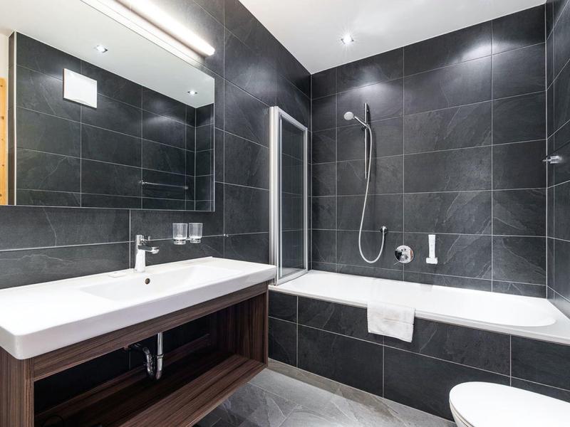 Modern bathroom with black tiles, white bathtub, and wooden vanity under sink.