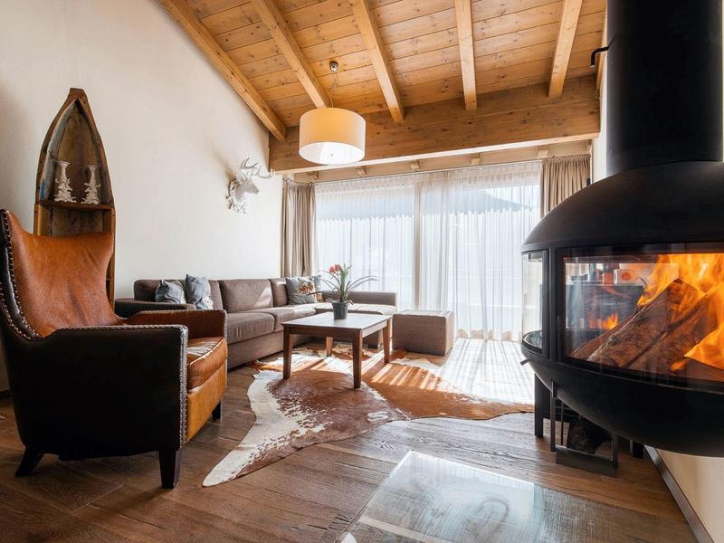 Cozy living room with wooden ceiling, leather chair, sofa, glass coffee table, and modern fireplace.