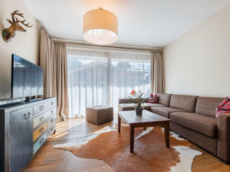 Modern living room with TV, brown sofa, coffee table, ottoman, and large window with curtains.
