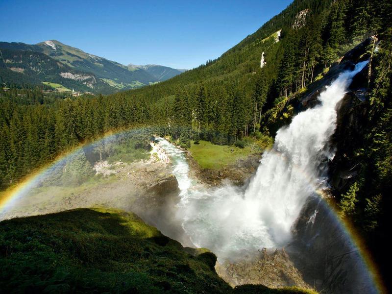 Waterfall in a lush forest with a rainbow in the mist and mountains in the background