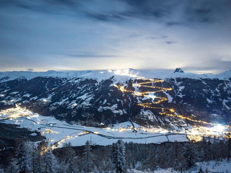 Snow-covered mountain village illuminated at night under cloudy sky