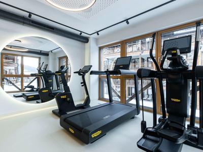 Moderner Fitnessraum mit Laufbändern, elliptischem Trainer, großen Fenstern und rundem Spiegel.