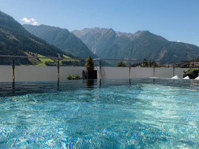 Blauer Pool mit klarem Wasser vor Glasgeländer, dahinter grüne Berge und blauer Himmel.