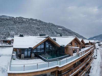 Modernes Hotel mit verschneitem Dach und Glasgeländer in winterlicher Berglandschaft.