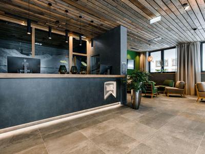 Moderner Empfangsbereich mit dunkler Theke, Holzdecke, großen Fenstern und gemütlichen Sitzplätzen.