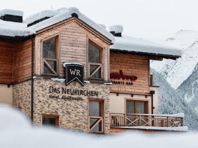 Alpenhotel mit Holz- und Steinfassade umgeben von Schnee und Bergen im Hintergrund.
