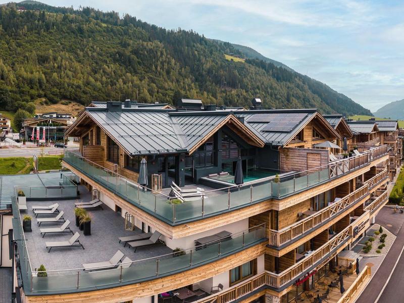 Modernes Holzhaus mit großer Dachterrasse in bergiger Landschaft bei bewölktem Himmel.