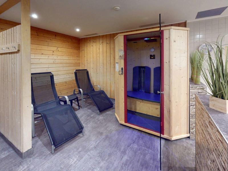 Pohodlná sauna s dřevěným obkladem, lehátky a moderním soláriem s červeným světlem.