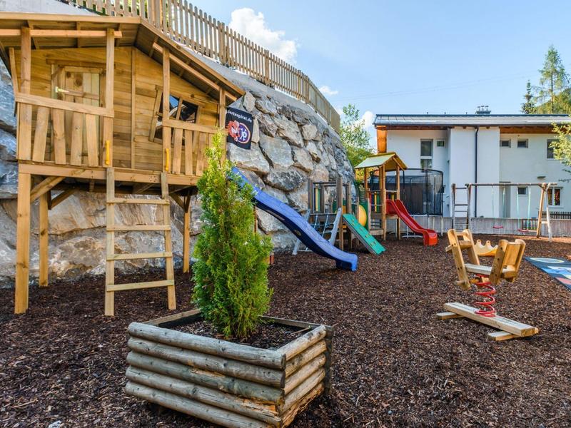 Children's playground with climbing frame, slide, and carousel next to a hotel building.