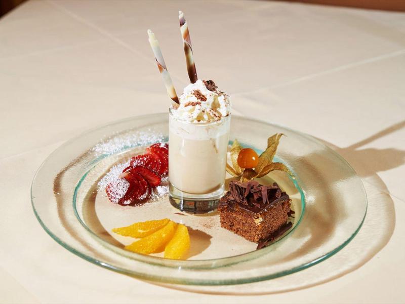 Small dessert plate with a whipped cream drink, chocolate brownie, cherries, and mango slices.