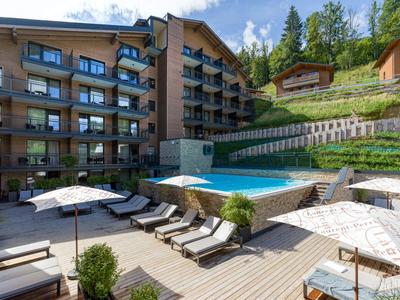 Hotel terrace with pool, lounge chairs, and umbrellas set against forested hills.
