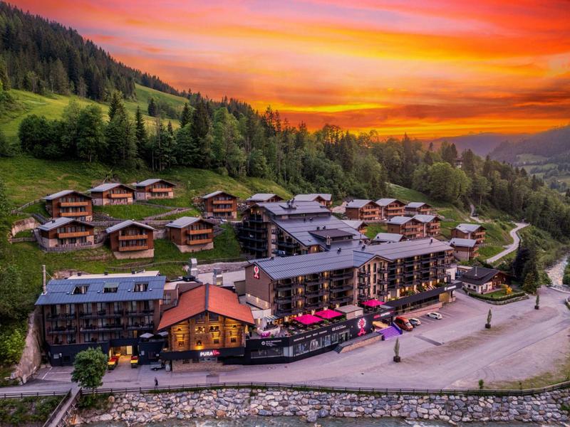 Mountain resort with chalets and main building against a vibrant sunset.