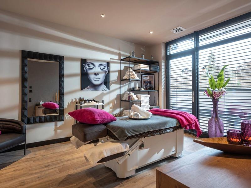 Modern wellness room with massage table, colorful cushions, and large windows.