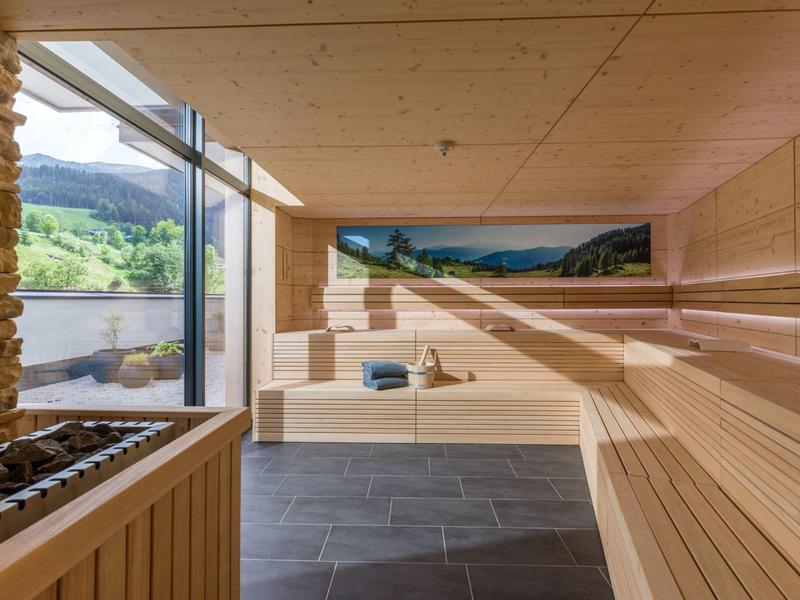 Modern sauna room with wooden benches, panoramic window showing green hills.
