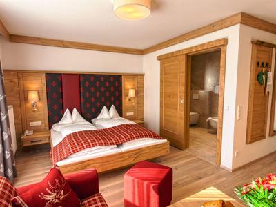 Gemütliches Schlafzimmer mit Holzmöbeln, Doppelbett, rotem Sofa und Zugang zum Badezimmer.