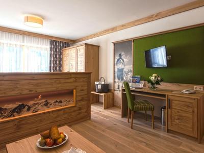 Gemütliches Zimmer mit Holzmöbeln, grünem Akzent und Schreibtisch unter Fernseher mit Fensterlicht.