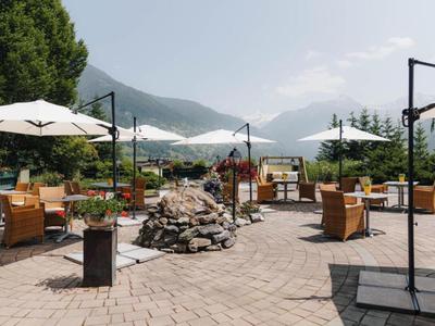 Außenbereich eines Restaurants mit Tischen, Stühlen und Sonnenschirmen vor Bergen.