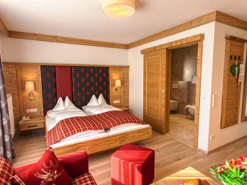 Gemütliches Schlafzimmer mit Holzmöbeln, Doppelbett, rotem Sofa und Zugang zum Badezimmer.