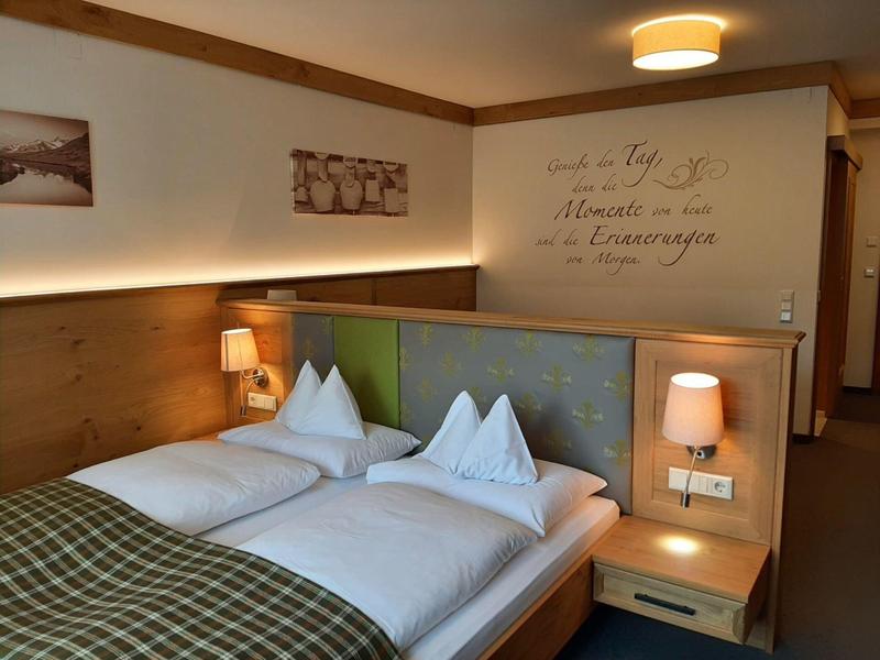 Gemütliches Doppelbett mit weißen Kissen, grüner Bettdecke und indirekter Wandbeleuchtung.