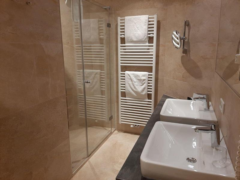 Modernes Badezimmer mit zwei weißen Waschbecken, Handtuchheizkörper und begehbarer Glasdusche.