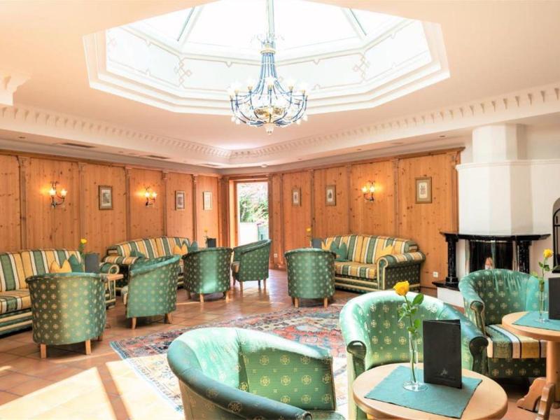 Eleganter Hotel-Lounge mit grünen Sesseln, Kamin und Kronleuchter unter einem Oberlicht.