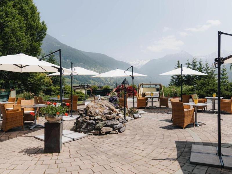 Außenbereich eines Restaurants mit Tischen, Stühlen und Sonnenschirmen vor Bergen.