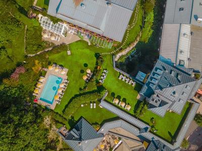 Aerial view of a hotel with a pool, sun loungers, green lawns, and pathways along water.