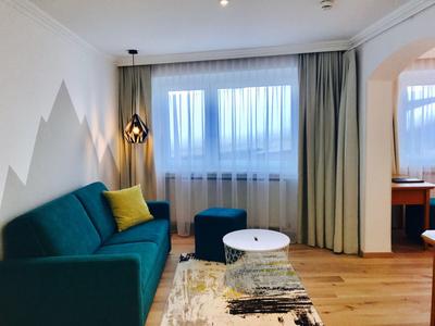 Cozy hotel room with teal sofa, yellow pillow, round ottoman, and wooden floor.