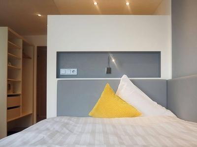 Modern hotel room with bed, gray headboard, yellow and white pillows, and built-in closet.