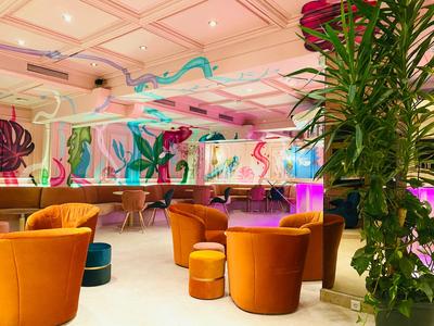 Sala moderna con sillones naranjas, plantas y decoración mural colorida en un hotel.