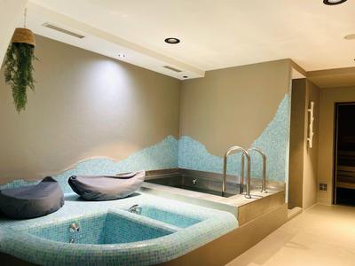 Indoor spa area with jacuzzi, comfortable cushions, and modern lighting in a beige room.