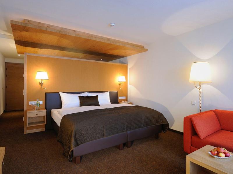 Hotel room with a large bed, wooden headboard, bedside lamps, a red sofa, and a floor lamp.