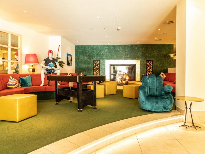 Hotel lounge with colorful seating, green carpet, foosball table, and modern decor