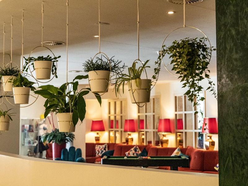 Indoor hanging plants above a modern lounge area with red lamps and seating.