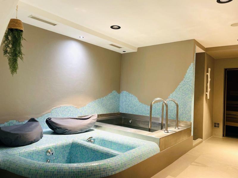 Indoor spa area with jacuzzi, comfortable cushions, and modern lighting in a beige room.