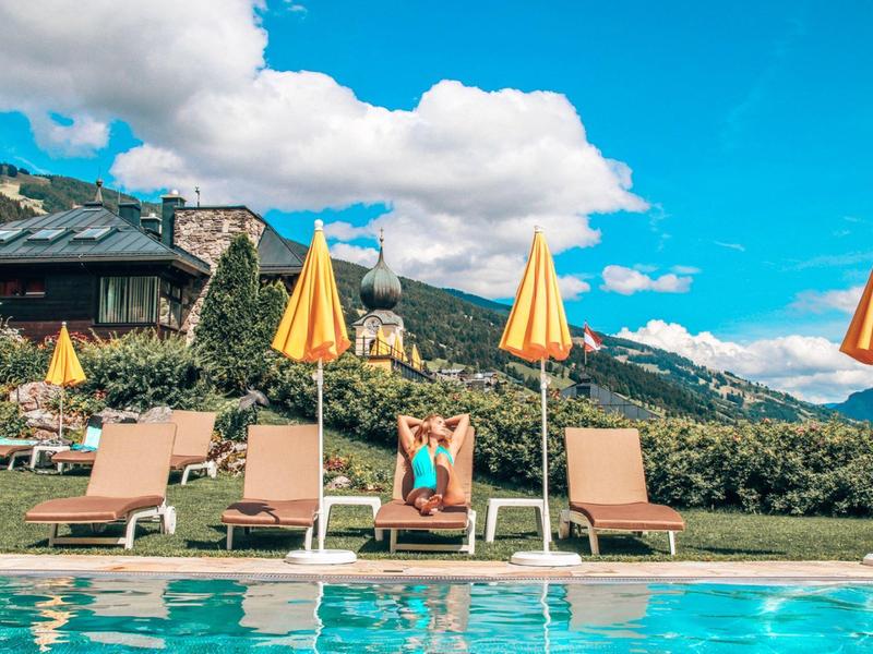 Sunny poolside with lounge chairs and yellow umbrellas near a mountain hotel.