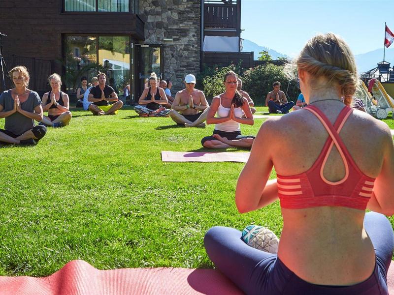 Group practicing outdoor yoga on green grass near modern building on sunny day.