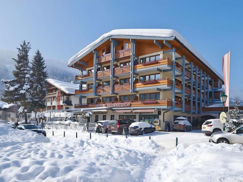 Großes Holzgebäude mit Balkonen, umgeben von Schnee und Autos unter klarem Himmel.