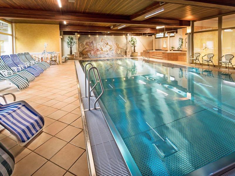 Hallenbad mit blauen Liegestühlen, großem Pool, Holzdecke und warmem Licht.