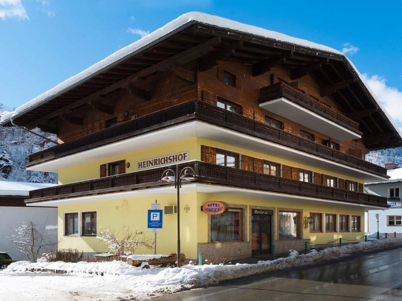 Traditionelles gelbes Alpenhaus mit Holzbalkonen und schneebedecktem Dach bei klarem Himmel.