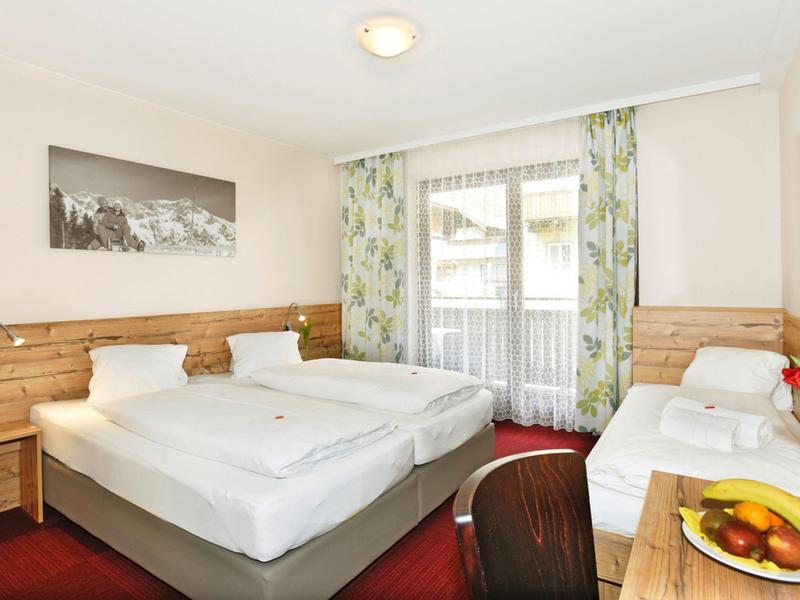 Gemütliches Hotelzimmer mit zwei Betten, Fenster mit Vorhängen, Schreibtisch und Obstschale.