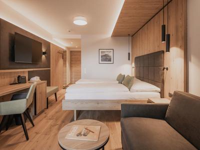 Modernes Hotelzimmer mit Doppelbett, Schreibtisch, Fernseher, Sofa und warmem Holzdekor.